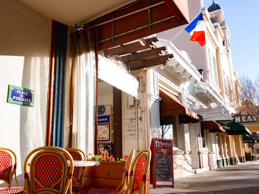 A French flag flies over sidewalk tables on the plaza