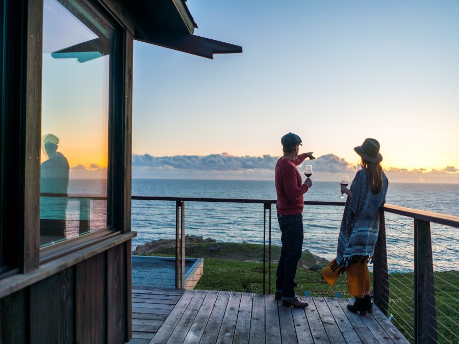 A couple looks out onto the ocean from a balcony in their suite