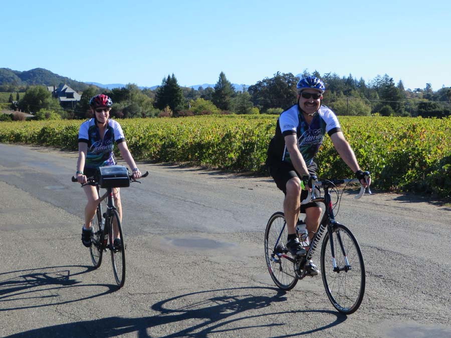 Two people cycle past vineyards