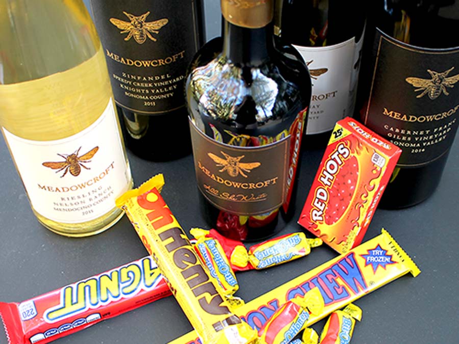 Bottles of red and white wine are lined up on a table withHalloween candy