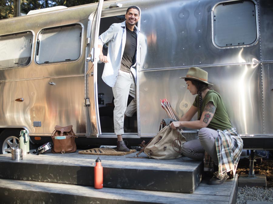 A person steps out of a metal airstream trailer beneath the redwoods