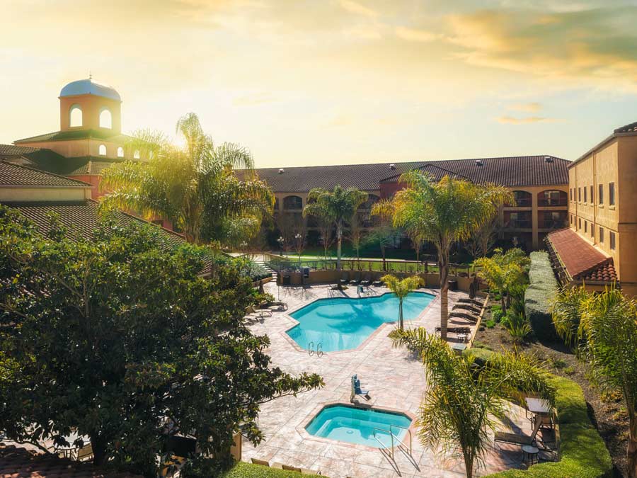 The pool at the Doubletree by Hilton Hotel Sonoma Wine Country is surrounded by palm trees at sunset in Sonoma County