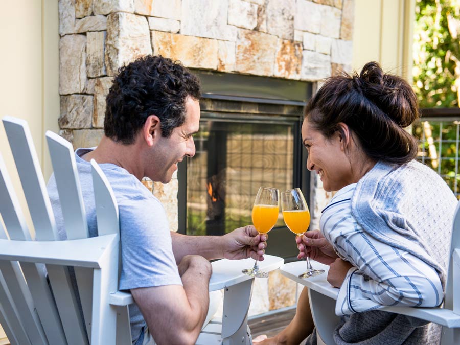 Two people sit in bath robes toasting with orange juice