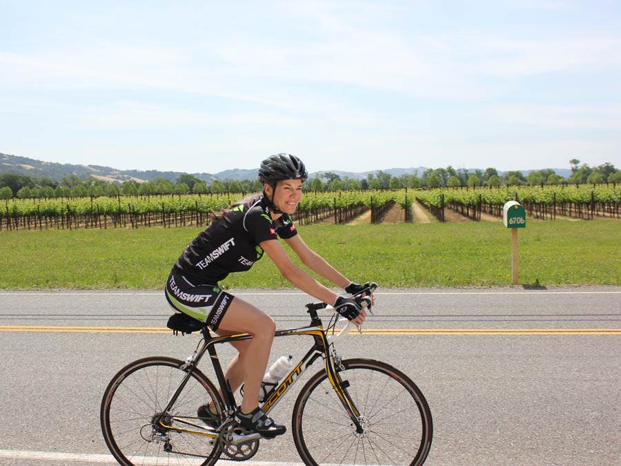 A woman cycles past rows of green vineyards