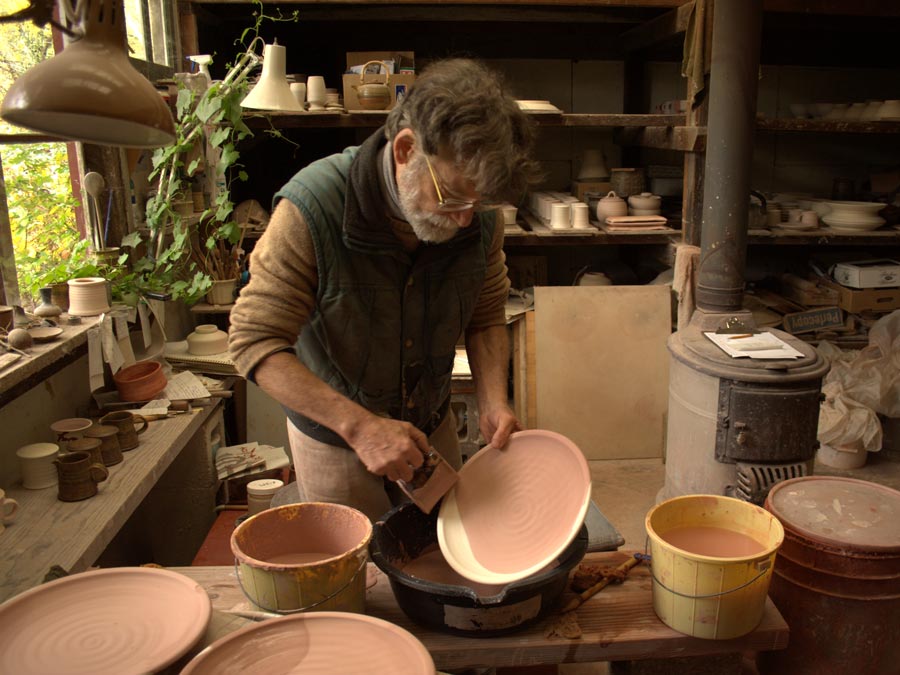 A person glazes pottery in their studio