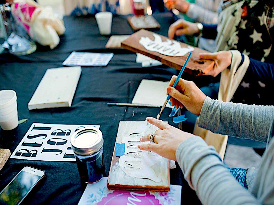 Hands of people stenciling wooden signs at a Boards & Bottle event