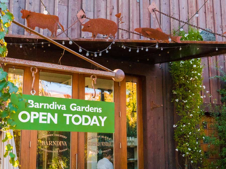 A sign in front of the rustic, barn says Barndiva Gardens Open Today