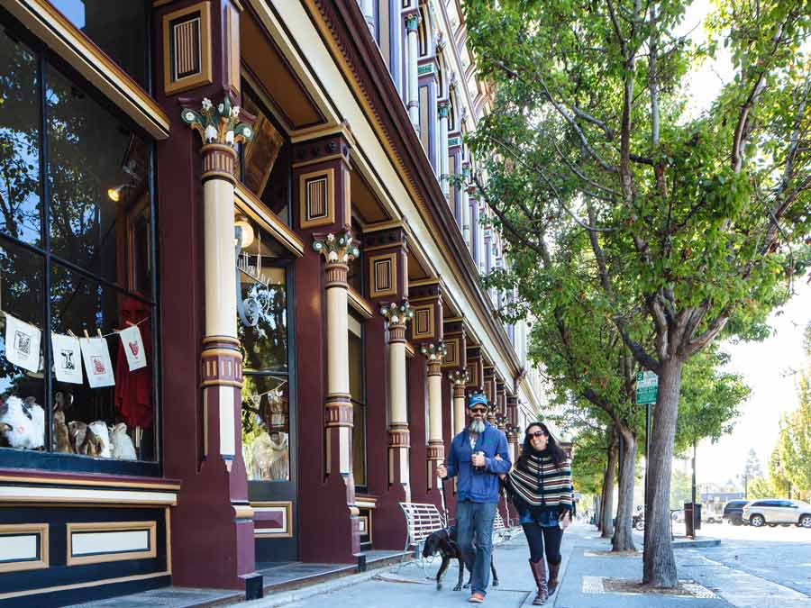 Two people walk with their dog next to Victorian buildings in downtown Petaluma, Sonoma County