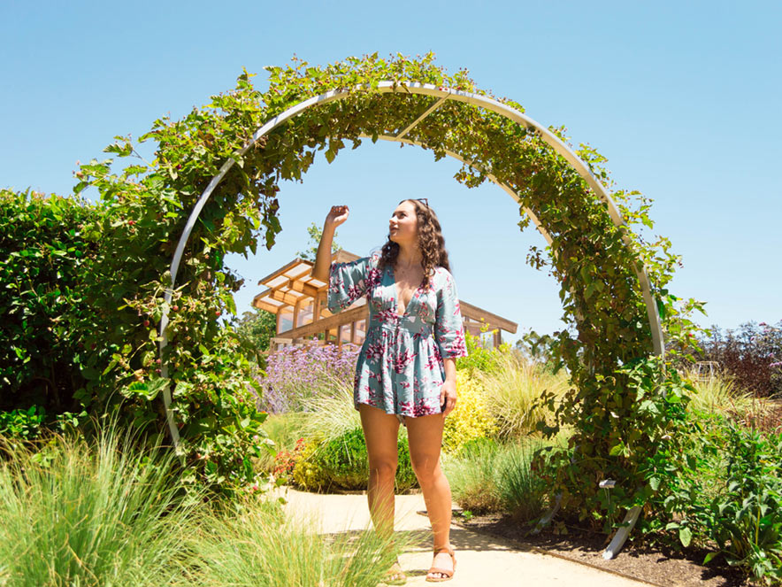 A woman poses for a photo under an arbor of flowers