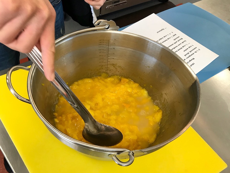 Yellow fruit jam being stirred in a silver bowl 