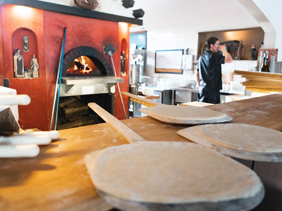 A chef stands next to the pizza oven where pizzass are ready to be cooked