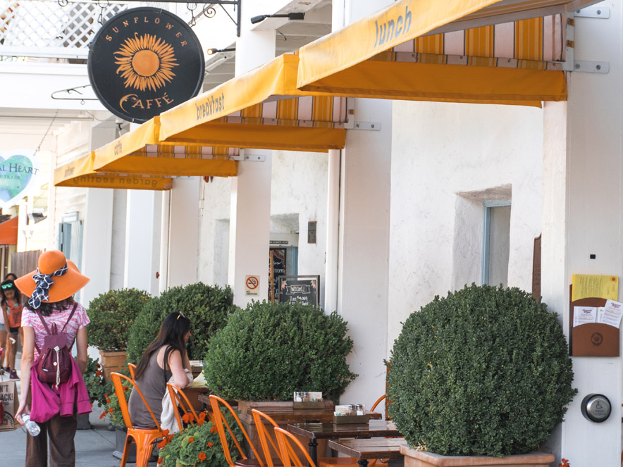 A person wearing a sun hat walks next to tables that line the plaza