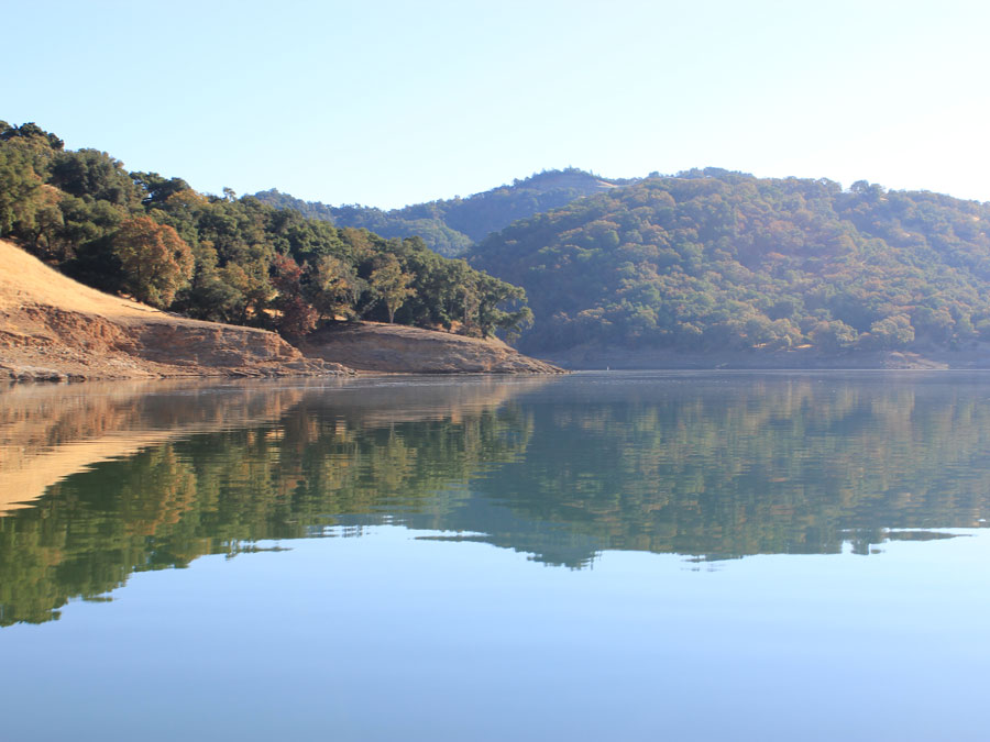 The hills and trees are reflected in the calm, blue water in the lake