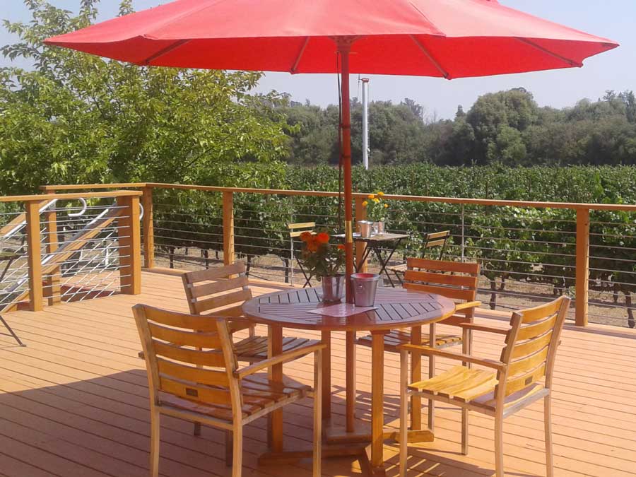 A teak table with a red umbrella on a deck overlooking vineyards