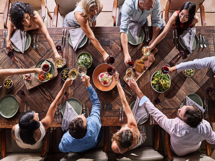 From overhead, a long table laden with food and wine, with diners toasting each other