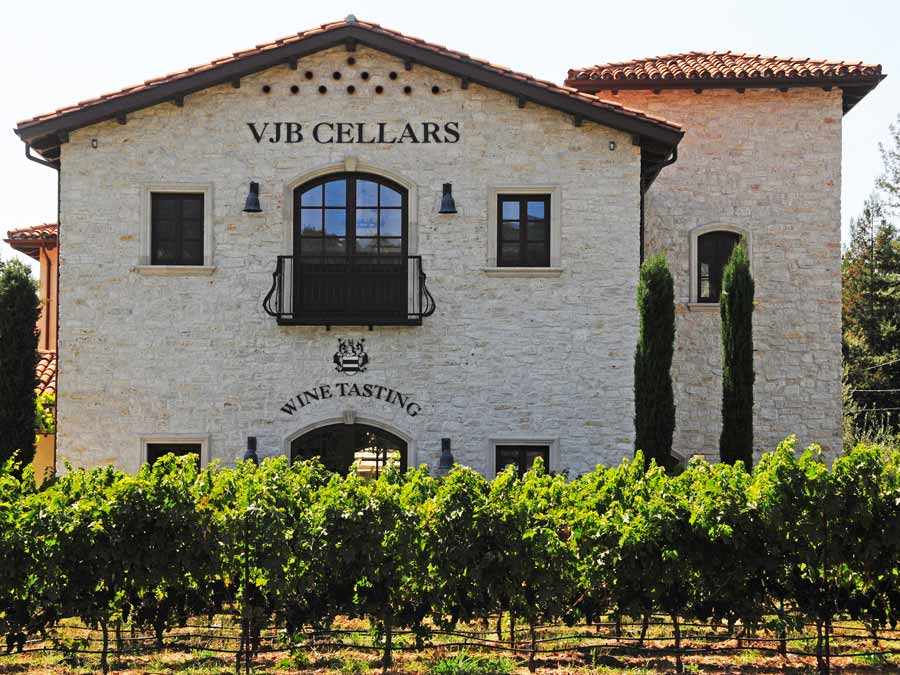 The exterior of the white stone winery is surrounded by hedges and vineyards