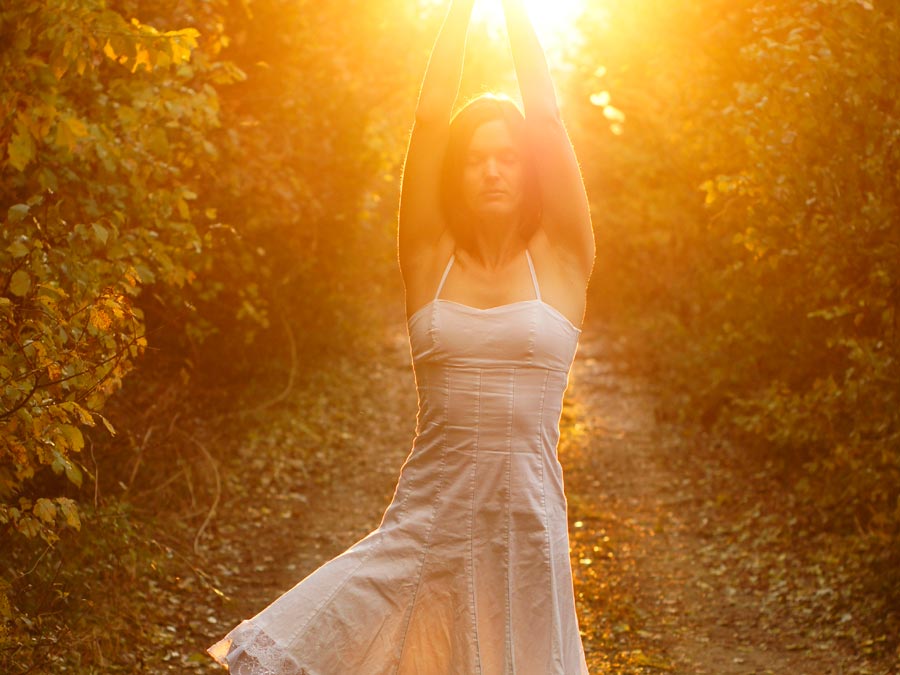 A woman stretches with the sun setting behind her among rown of grape vines