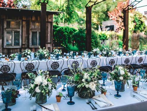 long table setting with blue glasses and black chairs in barn-like setting