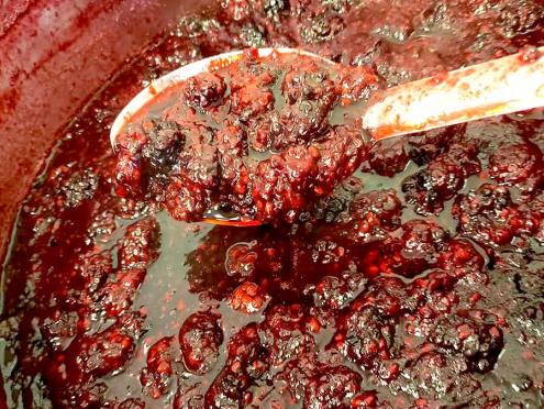 Close up of red berry jam being stirred in a bowl with a silver spoon