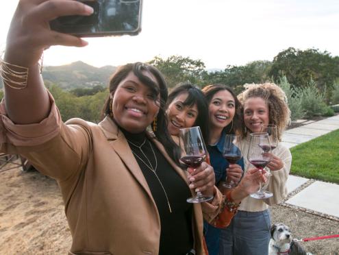 Women taking selfie in vineyard while drinking wine.